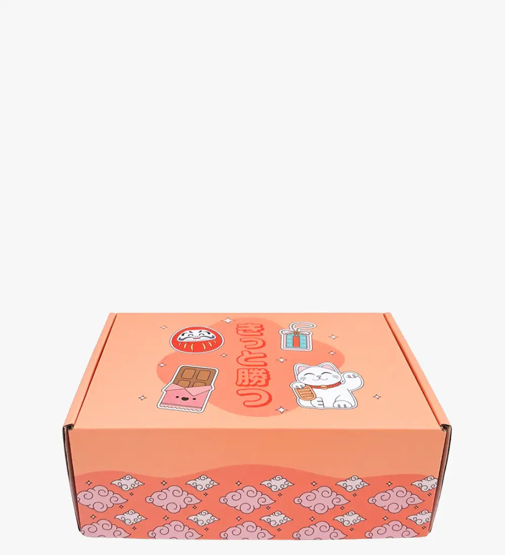 Caja de cartón de color coral con ilustraciones lindas de temática japonesa que incluyen un gato maneki blanco, una bola daruma y diseños de barras de chocolate.