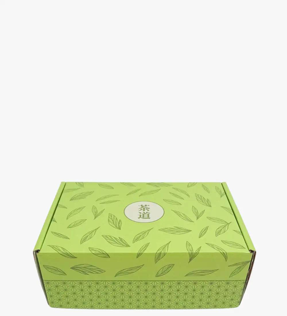 Caja de cartón verde lima adornada con un patrón repetitivo de hojas y que presenta los caracteres chinos '茶道' en un emblema circular central.