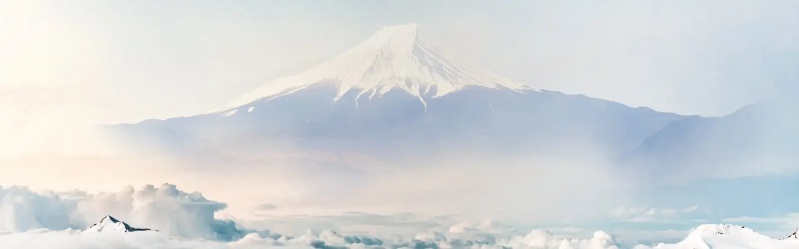 El monte Fuji con su cima nevada se eleva majestuosamente contra un cielo suave y brumoso.