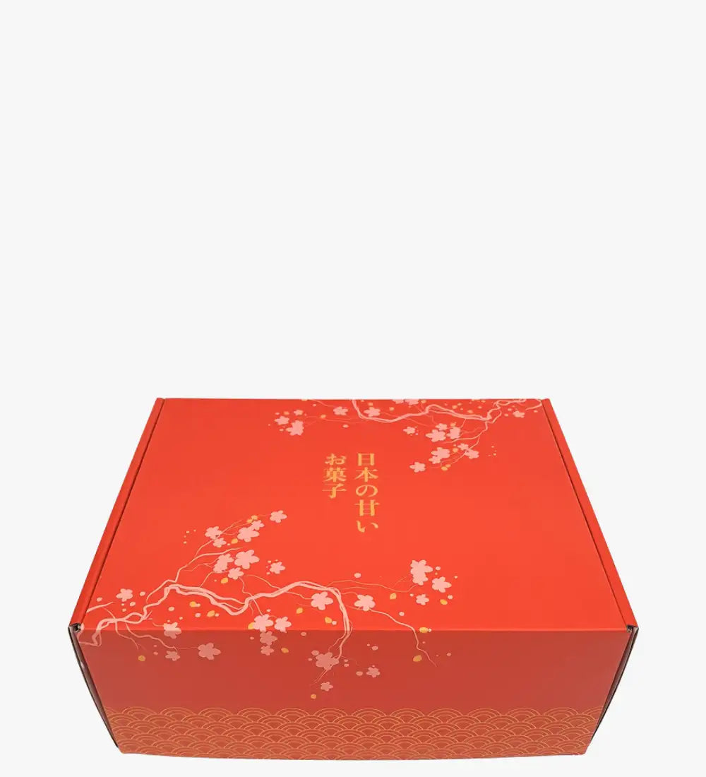 Caja de regalo de cartón rojo con delicados patrones de flores de cerezo blancas y hoja de oro, con texto japonés a lo largo del lado.